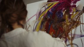Contemporary woman painter using palette knife in art studio. Back view of talented girl painting on canvas indoors. Inspired female artist creating artwork at workshop.