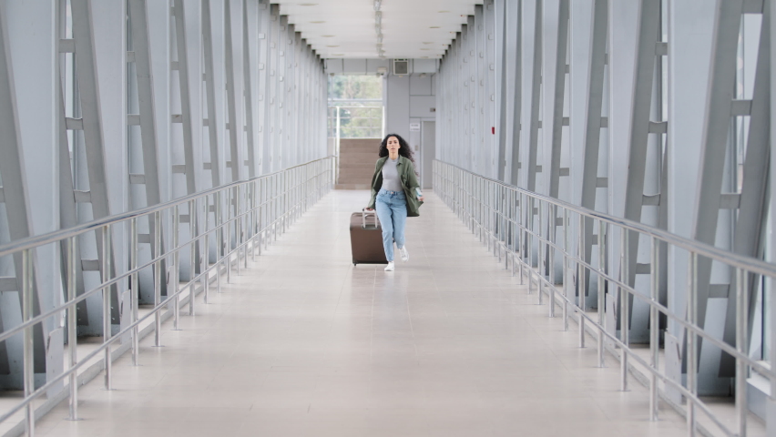 Young hispanic woman lady curly brunette girl passenger traveler with suitcase luggage runs in airport terminal hurrying late for plane landing flight holding train ticket and passport running worried Royalty-Free Stock Footage #1075277381