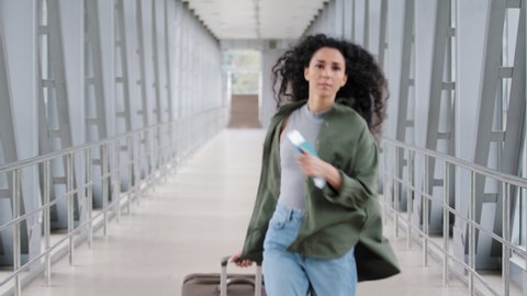 Young hispanic woman lady curly brunette girl passenger traveler with suitcase luggage runs in airport terminal hurrying late for plane landing flight holding train ticket and passport running worried