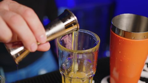 Professional bartender creating a cocktail drink. Experienced barman pouring alcohol beverage in glass before serving - food and drink concept close up.