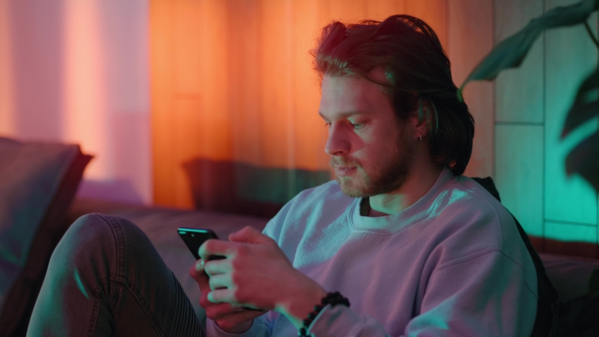 Handsome young man using smartphone social media, texting message and listening music, shaking head into rhythm enjoying home evening entertainment alone. Royalty-Free Stock Footage #1075283639