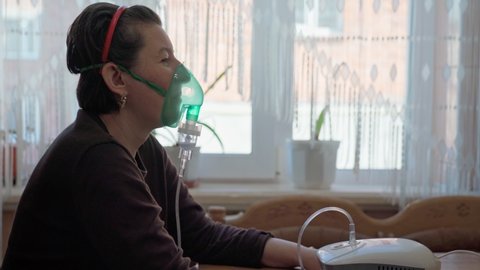 A European woman, at home, carries out inhalation, inhalation of oil vapors, oxygen through a mask. Treatment of pneumonia, bronchitis. Close-up.