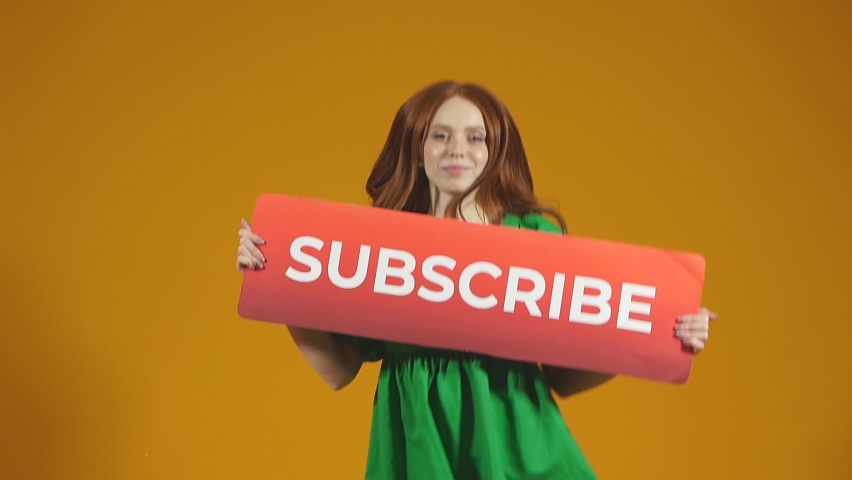 young red-haired female blogger jumping with a smile on an isolated background holds a sign to subscribe, she asks you to subscribe to her blog. slow motion