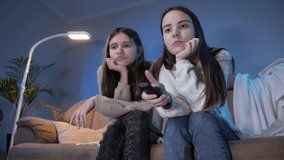 Two bored girls switching TV channels on remote controle while watching television at night