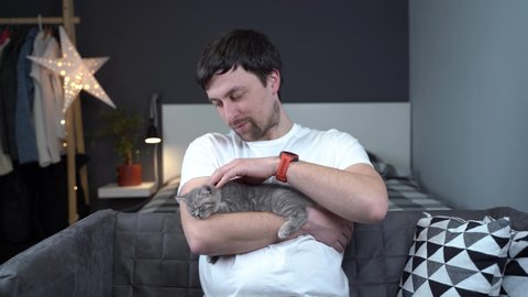 Pets love theme. Man gently protects sleep of kitten breed British prime-eared holding in arms and stroking at home. Lovely relationship between human and pet. Scottish straight gray kitten sleep