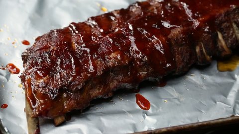 Brushing BBQ sauce on grilled rack of ribs on foil