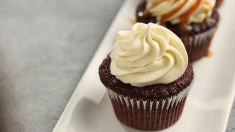 Drizzling caramel sauce on a chocolate cupcake with cream cheese frosting