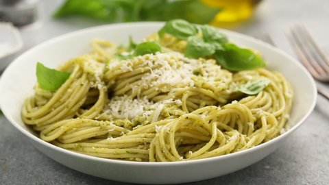 Basil pesto spaghetti pasta in a white bowl with parmesan, taking some pasta with a fork
