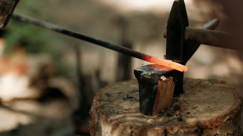 A blacksmith forges red-hot metal on an anvil. The hammer of smith beat on glowing hot metal and sparks fly in all directions. Metalworking. Blacksmithing Workshop.
