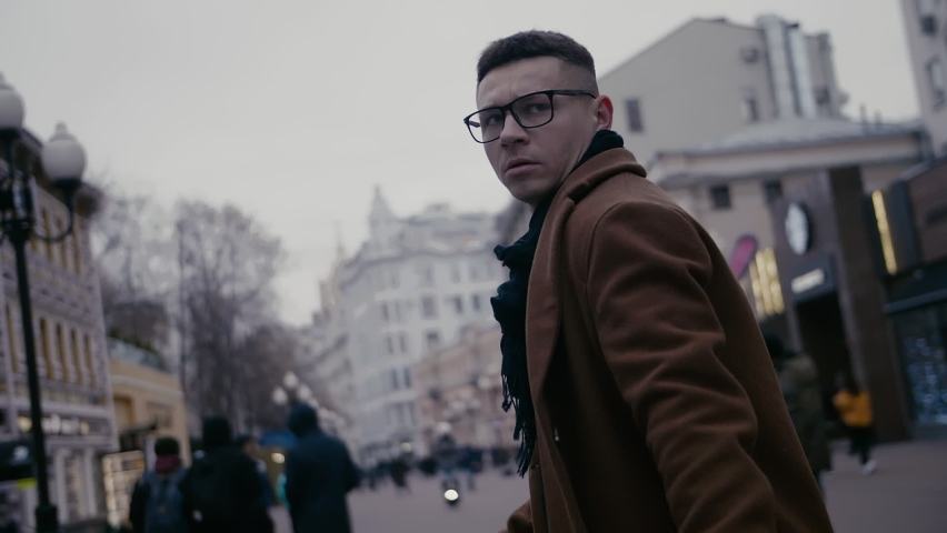 Young businessman goes and turns around along the city center street looks around city. He