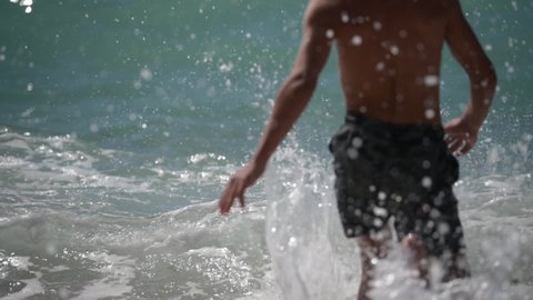 active little boy in shorts running to sea ocean water during storm with waves on holiday summer vacation