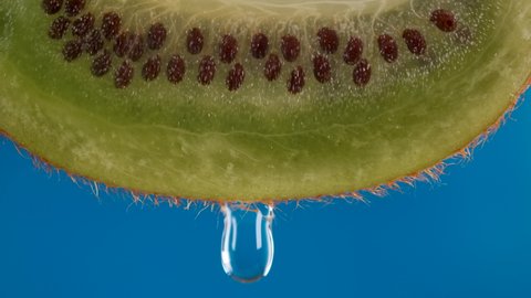 Macro Shot Drop Of Water Dripping Slice of fresh Green Kiwi and Seeds Fruit on Blue Background. Slow Motion Water Drop From Juicy Fresh Ripe Delicious Sliced Kiwi Fruit, Close-up Slow Motion.