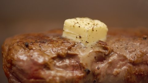 Butter, melting on small juicy pieces of fried beef meat, is sprinkled with aromatic spices, macro. Closeup