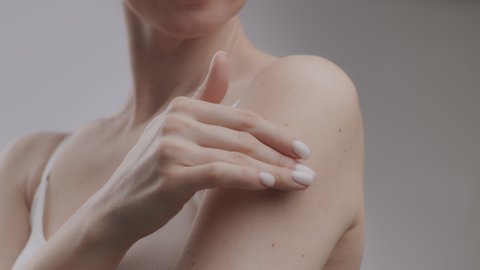 Female body pampering concept. Young unrecognizable caucasian woman applying moisturizing cream on her bare shoulder, bodycare procedures concept, slow motion