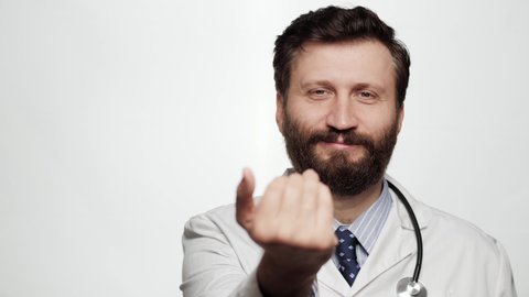 Doctor beckons with his palm. Portrait of smiling man doctor on white background looking at camera and beckoning, gesturing with his palm