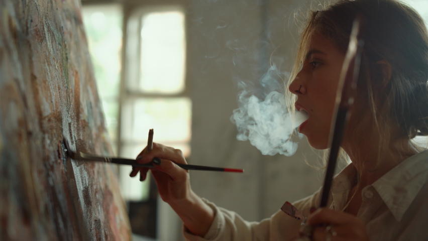 Talented woman painter exhaling cigarette smoke indoors. Inspired girl drawing with oil paints on canvas creative female artist creating masterpiece in art studio Royalty-Free Stock Footage #1075327898
