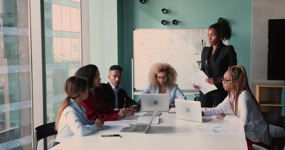Confident young african ethnicity businesswoman leading briefing meeting with motivated mixed race colleagues in modern office, discussing online project problem solution or developing growth strategy Royalty-Free Stock Footage #1075329932