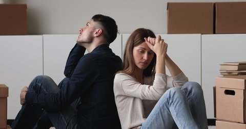 Sad couple leave house sit on floor back to back feel tired, heap of carton boxes with belongings near. Division of property, start living separately, divorce, hard move day, debt and eviction concept