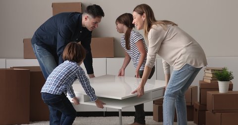 Happy family with children at relocation day carrying coffee table to living room together. Real estate, furniture replacement, life changes, remodelling services and modern apartment owners concept