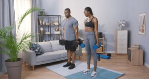 Full length view of the multiracial bearded man and his wife doing arms workout, while training with dumbbells at home. Sport and recreation concept. Stock video