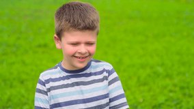 A beautiful boy of European appearance stands in a green field and laughs. The child demonstrates emotions of joy on his face. Slow-motion video, full hd. Place for text, Copyspace