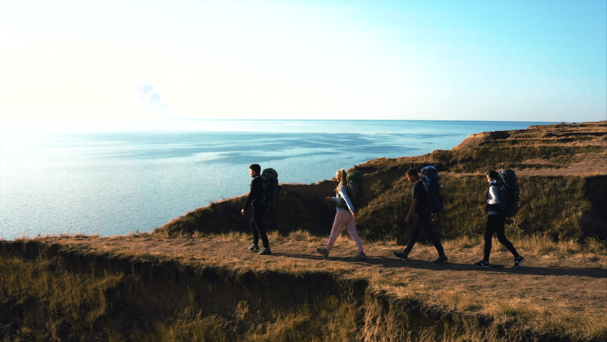 The tourists with backpacks walking on the mountain top near the sea