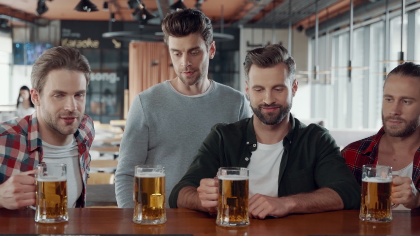 Happy young men in casual clothing toasting each other with beer the pub