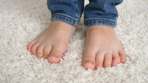Closeup of little barefoot boy standing on soft white carpet and moving toes.