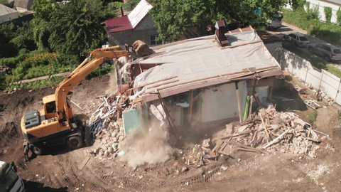 Demolition of old house building for new construction by excavator bucket, aerial view. City development