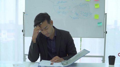 businessman checking documents stressed and tired in office. financial manager male carefully prepares a summary of the income. Young Asian man has a headache at work.