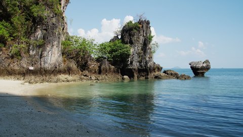 Emerald green waves gently lap onto the empty white sand beach of Hong Island, Krabi Thailand. Limestone karsts jut vertically out of the calm water at low tide in front of blue sky on a sunny day.