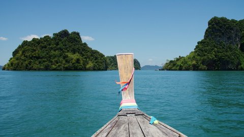 Traditional Longtail boat in Thailand speeds through the green waters of Phang Nga bay. Tree covered limestone karst dot the landscape on a clear sunny summer day.