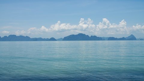 Limestone karsts dot the landscape of Phang Nga Bay, Phuket Thailand. The bright sun reflects on the blue turquoise water of the Andaman sea. Fluffy white clouds settle in the blue sky.