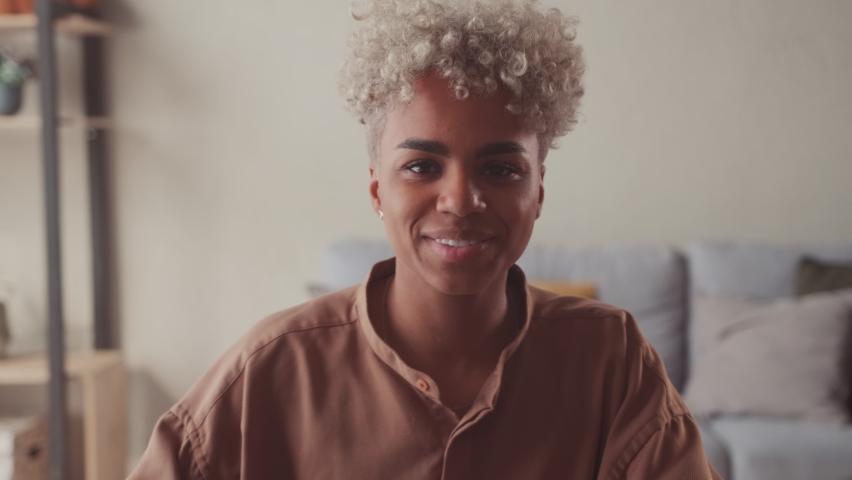 Happy young African American woman in casual wear looking at camera making hello welcoming gesture passing job interview distantly with employer, starting video call conversation with friends. Royalty-Free Stock Footage #1075351193