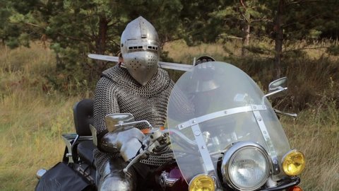 Kostanay, Kazakhstan, September 10, 2020. A medieval knight in full armor sits on a motorcycle against the backdrop of the forest.