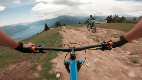 First person perspective of mountain biker descending hilly ridge line above iconic lake 