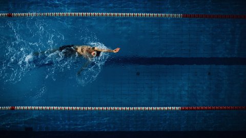 Aerial Top View: Male Swimmer in Swimming Pool. Professional Athlete Swims in Backstroke Style, Determination Win Championship. Dark Dramatic Colors, Cinematic Lap Lane Light. Aerial Slow Motion Shot