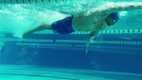 Underwater Shot: Fit Muscular Swimmer Diving, doing Laps in Swimming Pool. Handsome Professional Athlete swims at Great Speed. Ready To Set World Championship Record. Front View Colorful Artistic Shot