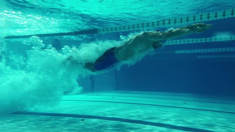 Underwater Shot: Fit Muscular Swimmer doing Laps in Swimming Pool. Handsome Professional Athlete swims at Great Speed. Ready To Set World Championship Record. Front View Colorful Artistic Stylish Shot