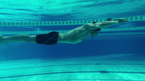 Underwater Shot: Fit Muscular Swimmer Jumps, Dives into Swimming Pool. handsome Professional Athlete swims at Great Speed- Ready To Set World Championship Record. Stylish Medium Shot