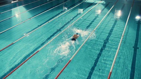 Aerial Top View Male Swimmer in Swimming Pool, Makes Laps with Record Setting Speed. Professional Athlete Training for Race, Winning World Championship Freestyle. Cinematic Wide Stationary Shot