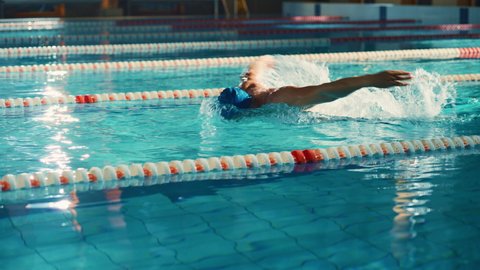 Successful Male Swimmer Racing, Swimming in Swimming Pool. Professional Athlete Determined to Win Championship using Butterfly Style. Colorful Cinematic Shot. Side View Tracking Slow Motion