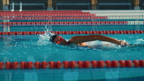 Successful Female Swimmer Racing in Swimming Pool. Professional Athlete Determined to Win Championship using Freestyle. Colorful Cinematic Shot. Side View Cinematic Tracking Shot Slow Motion