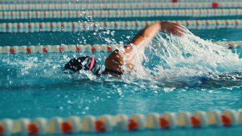 Successful Female Swimmer Racing in Swimming Pool. Professional Athlete Determined to Win Championship using Freestyle. Colorful Cinematic Shot. Side View Cinematic Tracking Shot