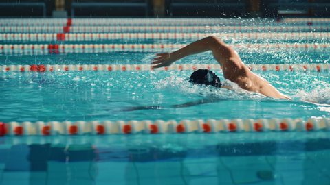 Successful Male Swimmer Racing, Swimming in Swimming Pool. Professional Athlete Determined to Win Championship using Front Crawl Freestyle. Colorful Cinematic Shot. Side View Tracking Slow Motion