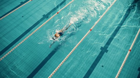 Aerial Top View: Beautiful Female Swimmer in Swimming Pool. Professional Athlete Swims in Freestyle Front Crawl Style. Determined Person in Training to Win Championship. Cinematic Tracking View