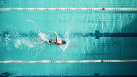 Aerial Top View: Muscular Male Swimmer Diving in Swimming Pool. Professional Athlete Gracefully Jumps, Swims Freestyle, Determined to Win Championship. Cinematic Tracking Slow Motion, Stylish Colors