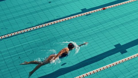 Beautiful Female Swimmer Using Front Crawl, Freestyle in Swimming Pool. Professional Athlete Determined to Win Championship. Cinematic Slow Motion, Stylish Colors, Artistic High Angle Tracking Shot