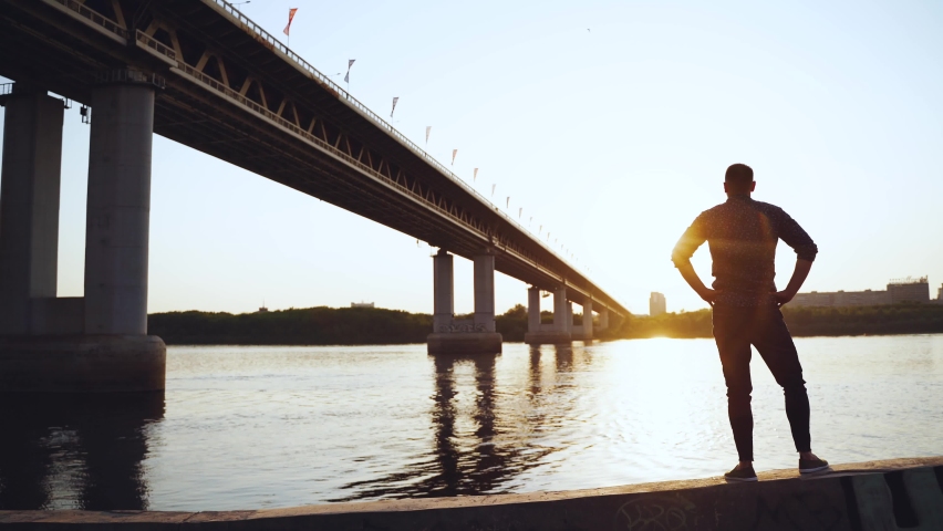 The silhouette of a man against the background of the bridge at sunset
