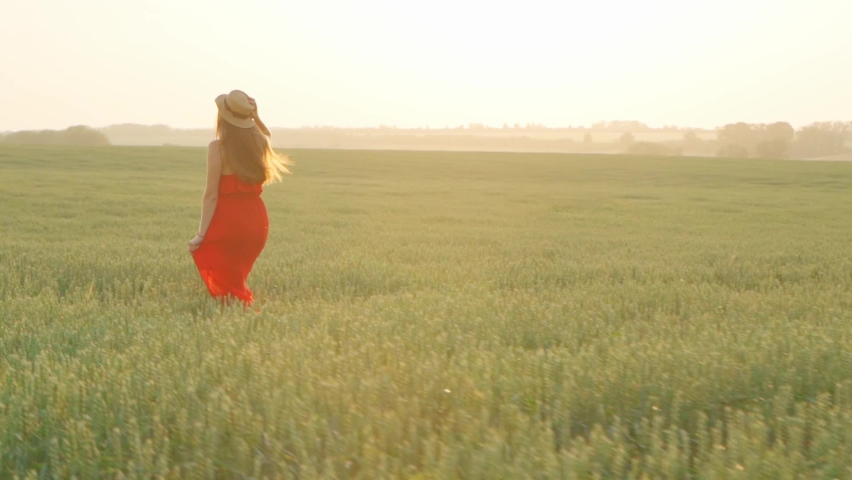 Girl in a red dress in a wheat field at sunset